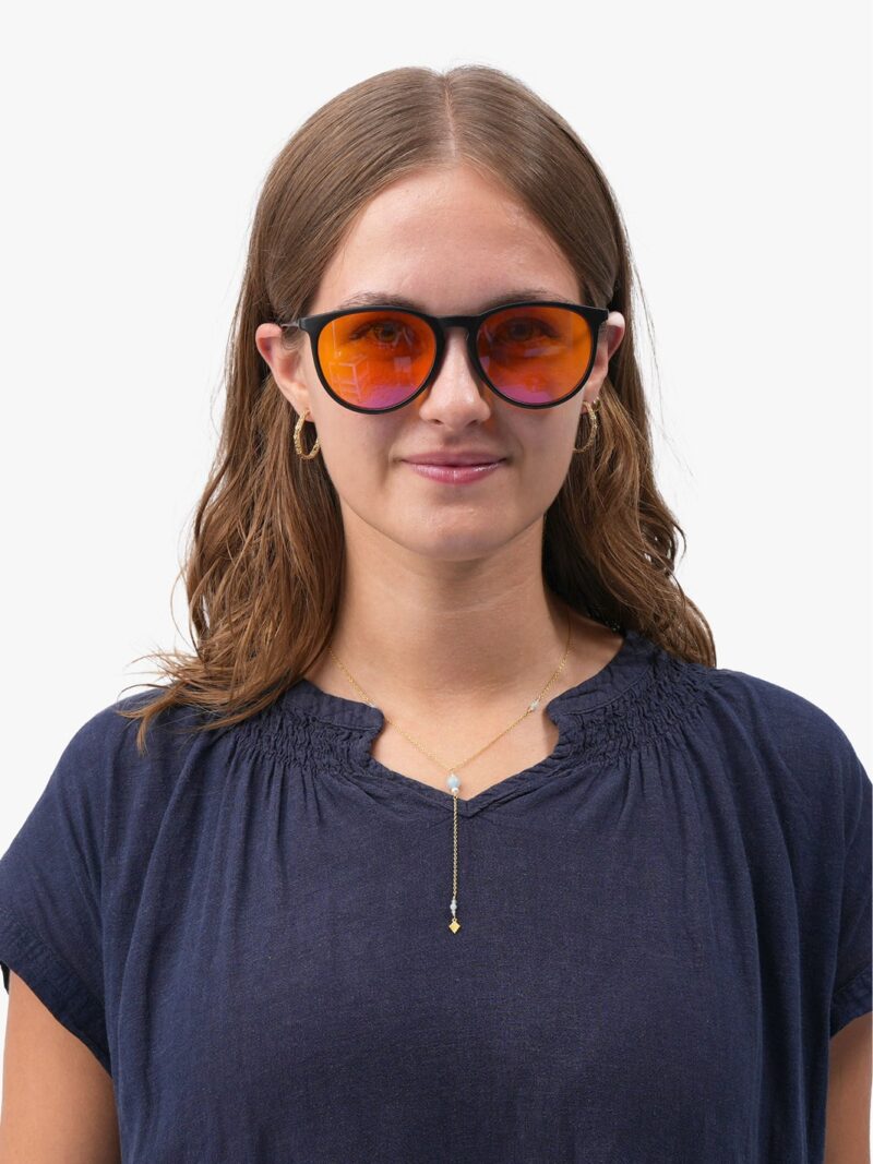 Frau in dunkelblauer Bluse mit schwarzer Brille mit orange verspiegelten Gläsern, goldener Halskette und goldenen Creolen