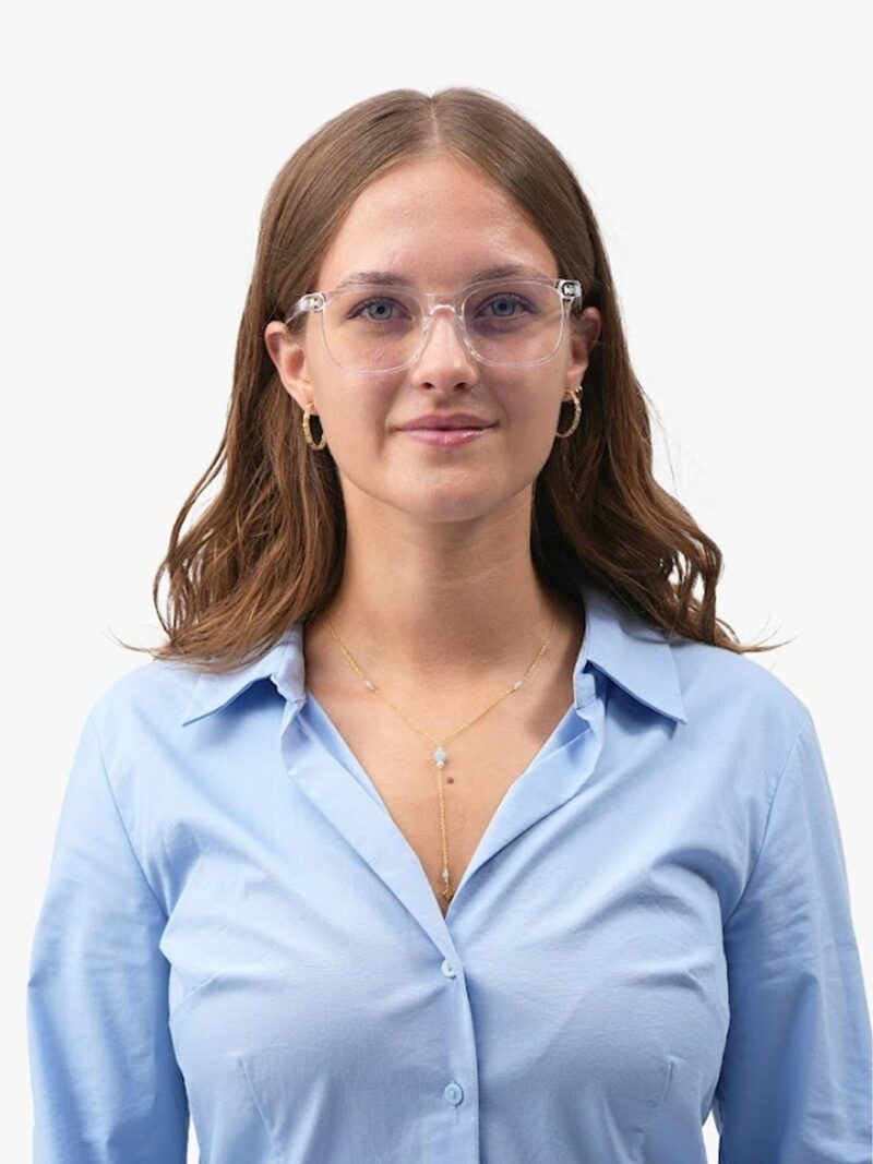 Junge Frau mit klarer Brille, goldenen Creolen, zarter Goldkette und hellblauem Hemd, sanftes Lächeln