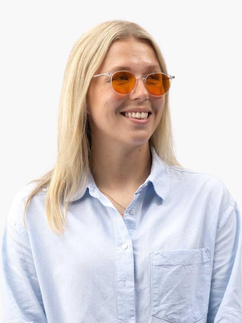 Lächelnde Frau mit langem blondem Haar, transparenter Fassung mit orangefarbenen Gläsern und hellblauem Hemd