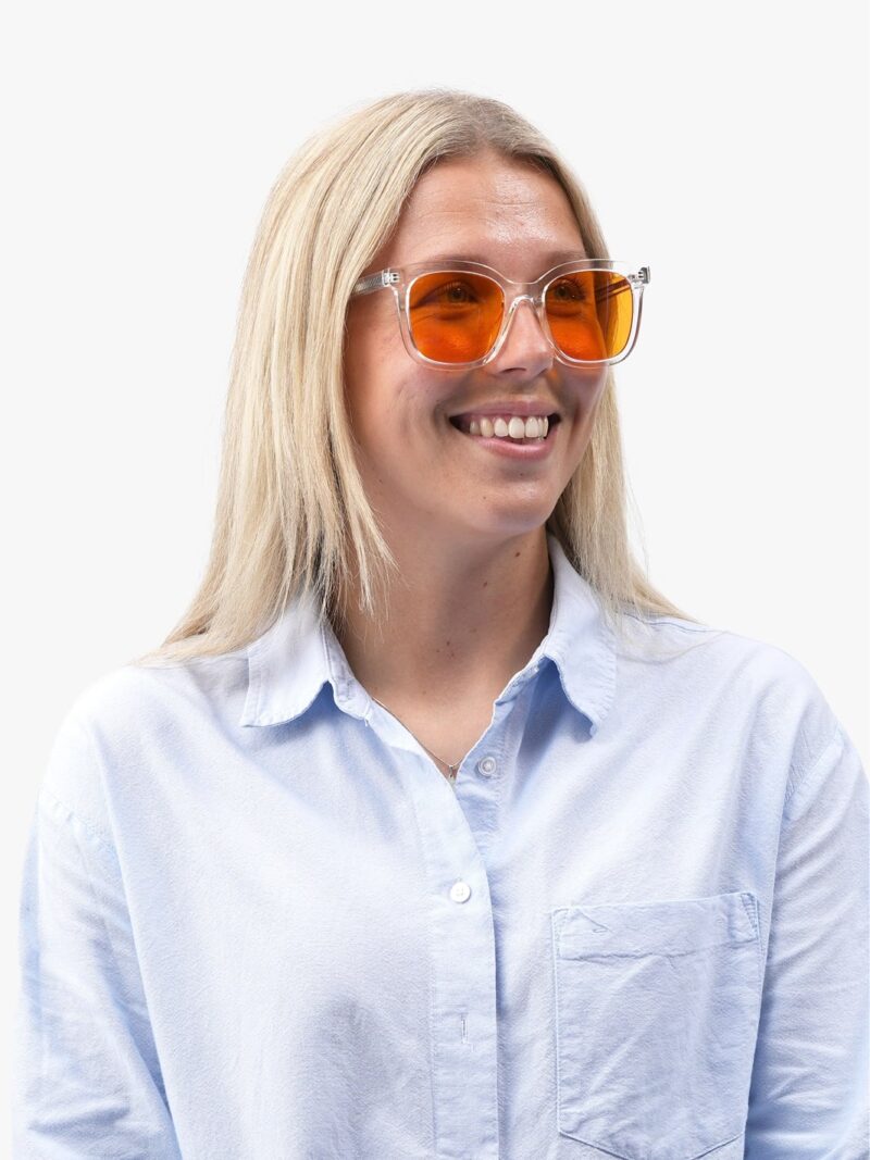 Lächelnde blonde Frau mit transparenter Sonnenbrille mit orangefarbenen Gläsern und hellblauer Bluse