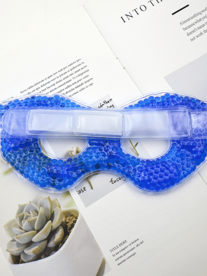 Kühlende blaue Gel-Augenmaske mit Perlen auf aufgelegten Magazinseiten