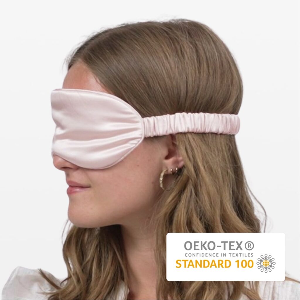 Seitenprofil einer Frau mit rosa Seidenschlafmaske, elastischem Band und goldenen Creolen, OEKO-TEX Standard 100